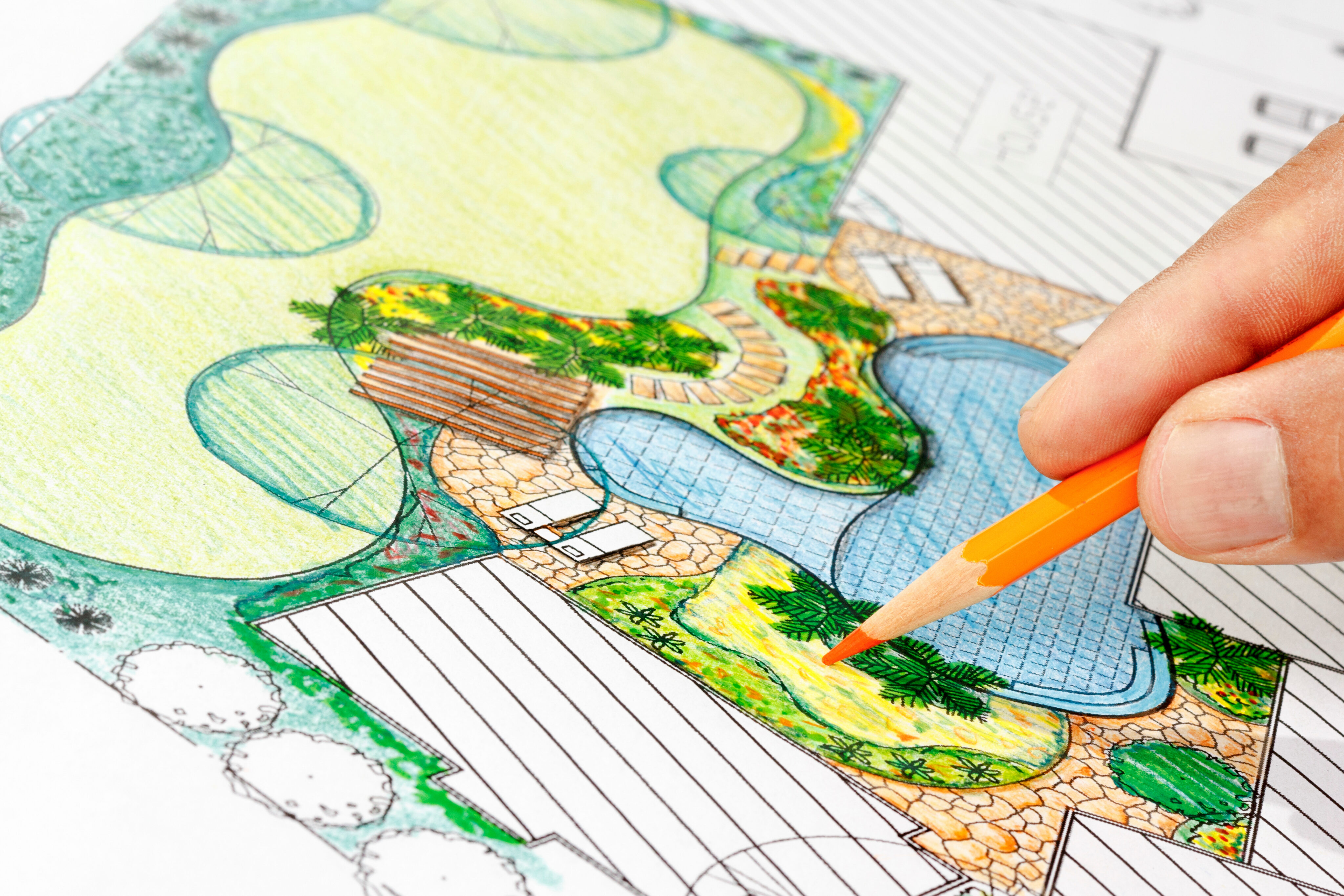 Close-up of a hand drawing a colorful landscape design plan, featuring shaded areas, plants, paths, and a pool layout. - Four Seasons Landscaping